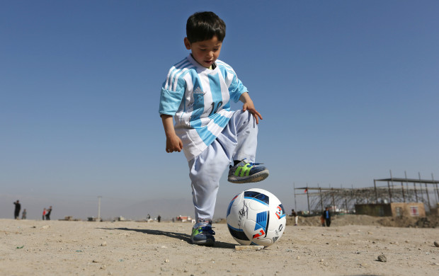 FILE - In this Friday, Feb. 26, 2016 file photo, Murtaza Ahmadi, a five-year-old Afghan Lionel Messi fan plays with a soccer ball during a photo opportunity as he wears a shirt signed by Messi, in Kabul, Afghanistan. The father of Ahmadi says the family was forced to leave Afghanistan amid constant telephone threats. (AP Photo/Rahmat Gul, File)