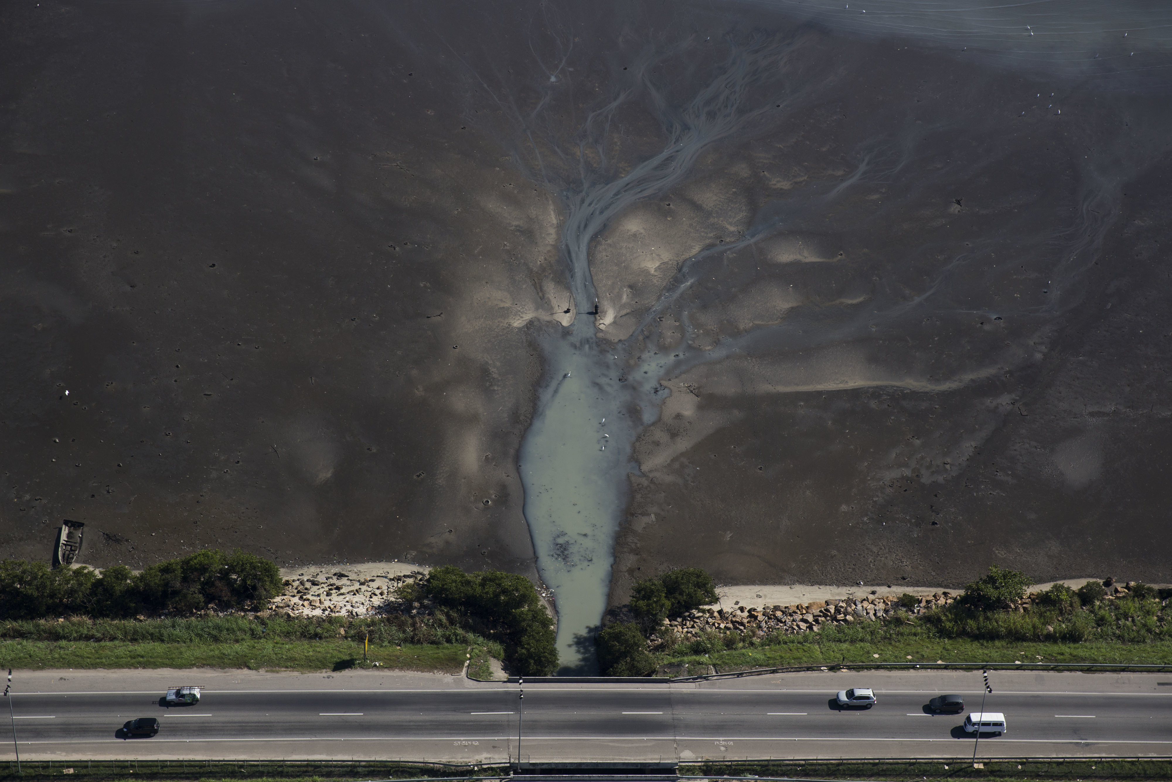 In this July 5, 2016 photo, cars drive above sewage flowing from the suburb of Sao Goncalo into Guanabara Bay, across the bay from Rio de Janeiro, Brazil. AP