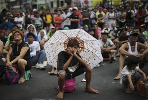 A Filipino uses an umbrella to shield him from the sun as they watch a live satellite feed of the welterweight title fight between Filipino boxing hero Manny Pacquiao and Floyd Mayweather Jr. during a free public viewing in downtown Manila, Philippines on Sunday, May 3, 2015. 