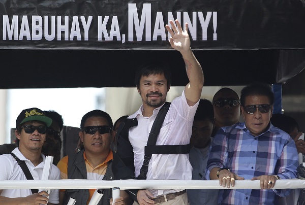 Filipino boxing hero Manny Pacquiao, wearing a black shoulder brace and arm sling, waves during a welcome motorcade in Manila, Philippines on Wednesday, May 13, 2015. Pacquiao returned home to the Philippines on Wednesday nursing his right shoulder after surgery and weighing up whether to retire or push for a rematch with Floyd Mayweather Jr. AP
