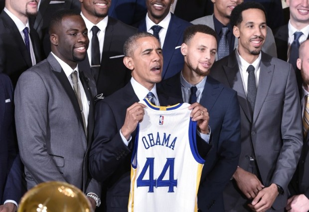 US President Barack Obama holds a jersey while poseing with  forward Draymond Green (L), Golden State Warriors guard Stephen Curry (2nd R) and guard Shaun Livingston (R) during an event honoring the 2015 NBA Champion Golden State Warriors in the East Room of the White House on February 4, 2015 in Washington, DC. / AFP / MANDEL NGAN