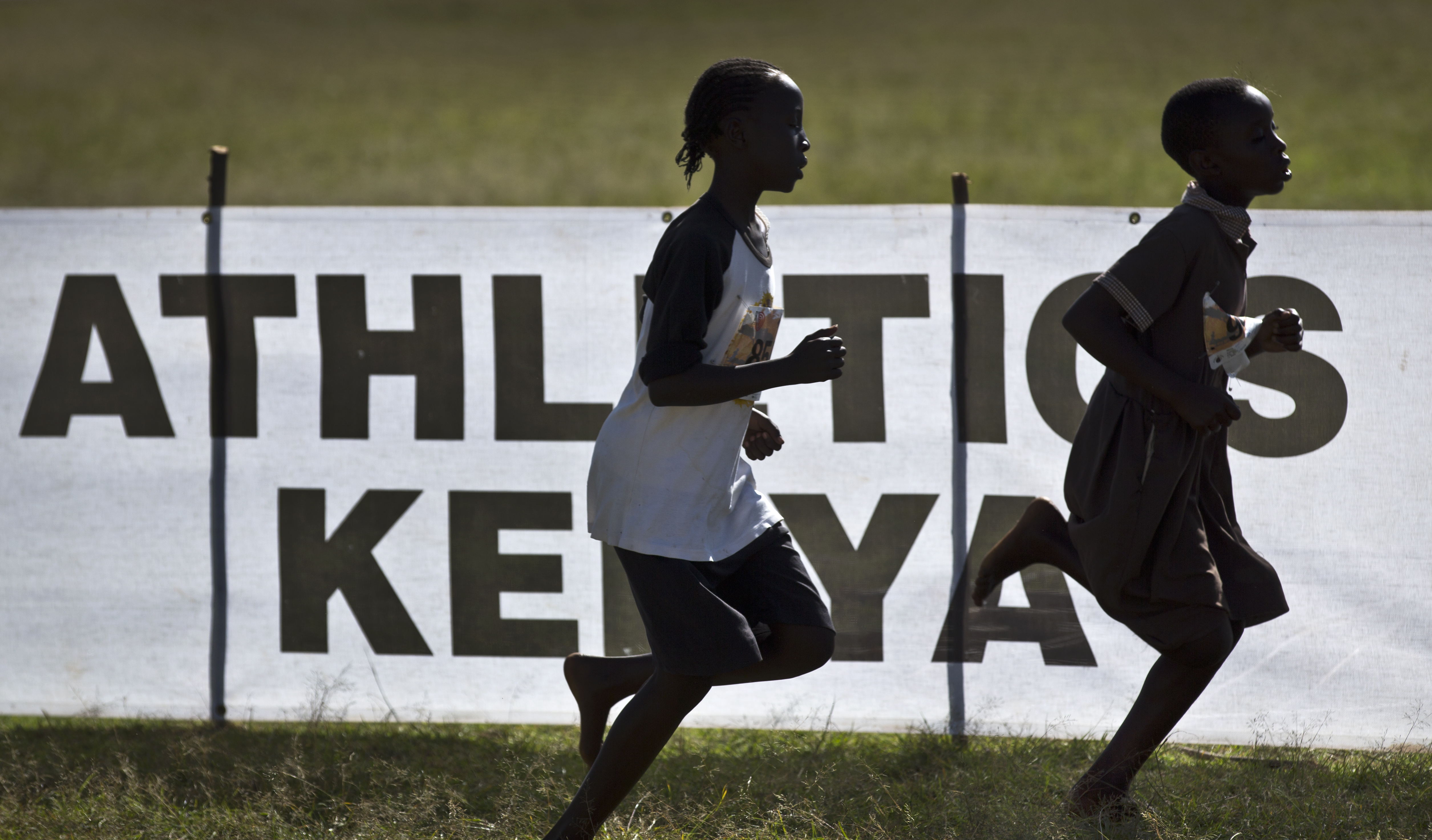 In this photo taken Sunday, Jan. 31, 2016, junior athletes run past a sign for Athletics Kenya at the Discovery cross country races in Eldoret, western Kenya.  AP