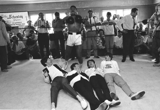 FILE - In this Feb. 18, 1964, file photo, boxer Muhammad Ali, or Cassius Clay at the time, beats his chest in triumph after toppling Britain's Beatles at his training camp in Miam i Beach, Fla. The Beatles, left to right: Paul McCartney; John Lennon; George Harrison and Ringo Starr, were on Holiday in the resort after their American tour.    Ali, the magnificent heavyweight champion whose fast fists and irrepressible personality transcended sports and captivated the world, has died according to a statement released by his family Friday, June 3, 2016. He was 74. (AP Photo/File)