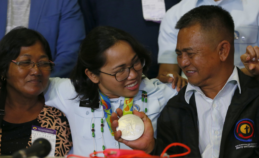 Hidilyn Diaz, center, who won Silver in the women's 53-kg Weightlifting in the Rio Olympics poses with her parents Emelita and Eduardo Sr. following a news conference upon arrival Thursday, Aug. 11, 2016, at the Ninoy Aquino International Airport in suburban Pasay city south of Manila, Philippines. The medal was the highest and the first for the Philippines in 20 years. Diaz dedicated her win to her mother.(AP Photo/Bullit Marquez)