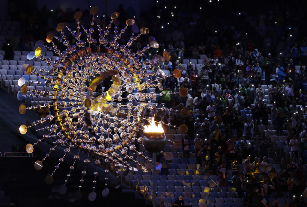 Spectators sit beside the cauldron with the Olympic flame prior to the closing ceremony in the Maracana stadium at the 2016 Summer Olympics in Rio de Janeiro, Brazil, Sunday, Aug. 21, 2016. (AP Photo/Natacha Pisarenko)