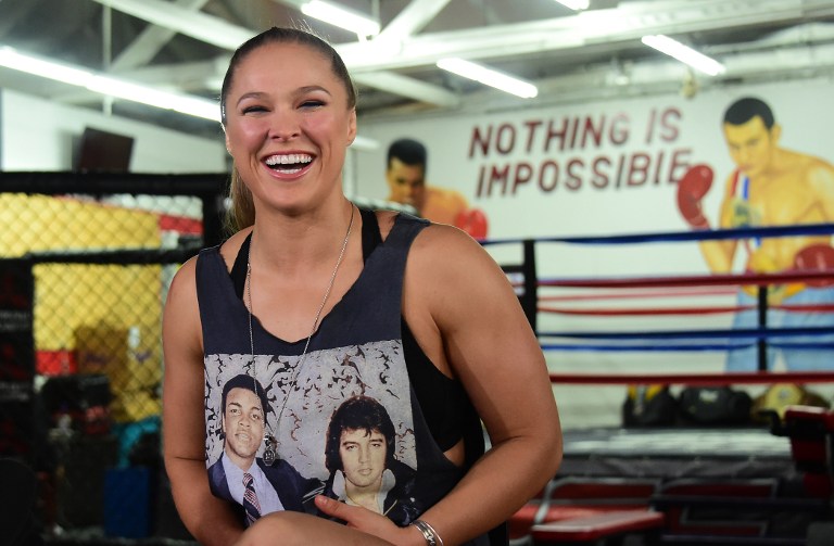 MMA fighter Ronda Rousey, wearing a shirt with portraits of former heavyweight  boxing champion Muhammad Ali (L) and the late US singer Elvis Presley (R),  responds to questions during media day in Glendale, California on October 27, 2015 ahead of her November 14 fight in Melbourne, Australia against Holly Holm. AFP PHOTO / FREDERIC J. BROWN / AFP PHOTO / FREDERIC J. BROWN