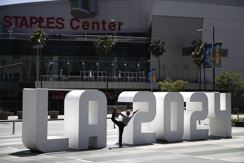Yoga instructor Michael Phillip poses with a Los Angeles 2024 sign outside Staples Center, Friday, May 12, 2017, in Los Angeles. (AP Photo/Jae C. Hong)