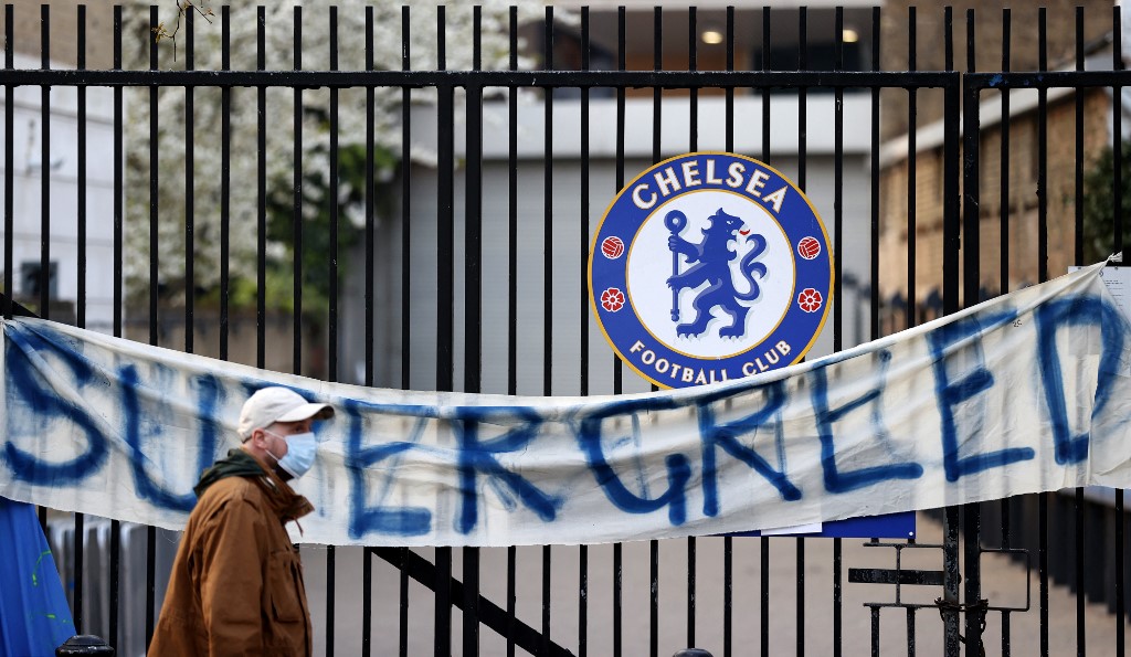 A pedestrian walks past an anti-European Super League banner reading "Supergreed" outside an entrance to Stamford Bridge football stadium in London