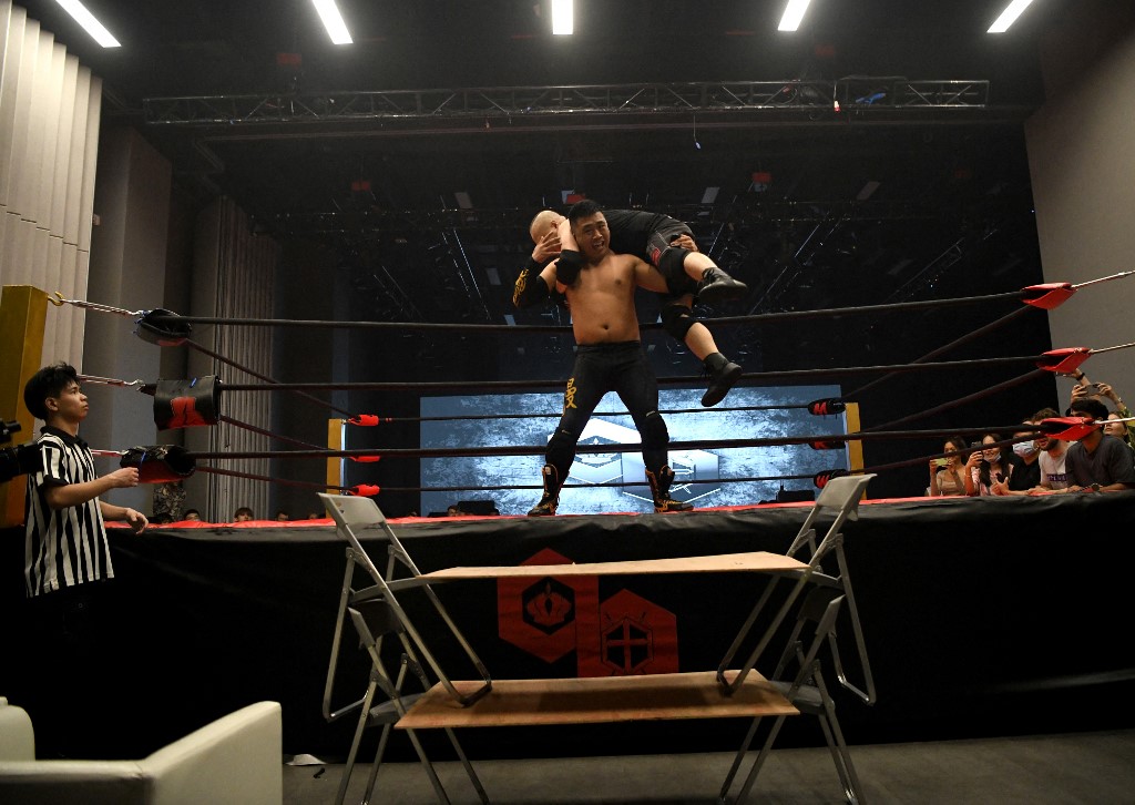 This photo taken on May 25, 2021 shows wrestler "Black Mamba", whose real name is Zhang Wendong, carrying "The Slam" on his back during their match at a Middle Kingdom Wrestling (MKW) event in the southern Chinese city of Shenzhen in Guangdong province. - The crowd gasps and cheers as a bare-chested man grabs a chair and smashes it over the head of his opponent on the ground; a referee in a black-and-white striped jersey rushes to his aid but the prone man is not really hurt -- this is WWE-style wrestling in China, where the sport is attempting to take off. (Photo by NOEL CELIS / AFP)