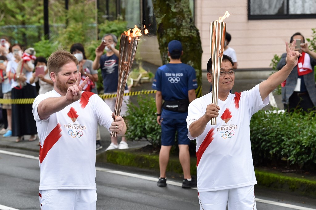Torchbearers Australian Shaun Ballinger (L) and Japanese Atsushi Kawaguchi (R) prepare to hand over the flame of the Olympic torch during the Tokyo 2020 Olympic Games Torch Relay in Gotemba, Shizuoka prefecture on June 25, 2021. (