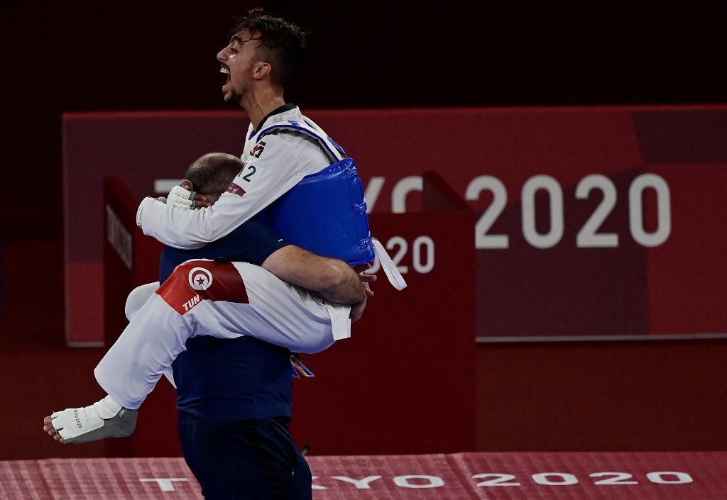 Tunisia's Mohamed Khalil Jendoubi (Blue) celebrates with his coach after winning the taekwondo men's -58kg semi-final bout against South Korea's Jang Jun (Red) during the Tokyo 2020 Olympic Games at the Makuhari Messe Hall in Tokyo on July 24, 2021.