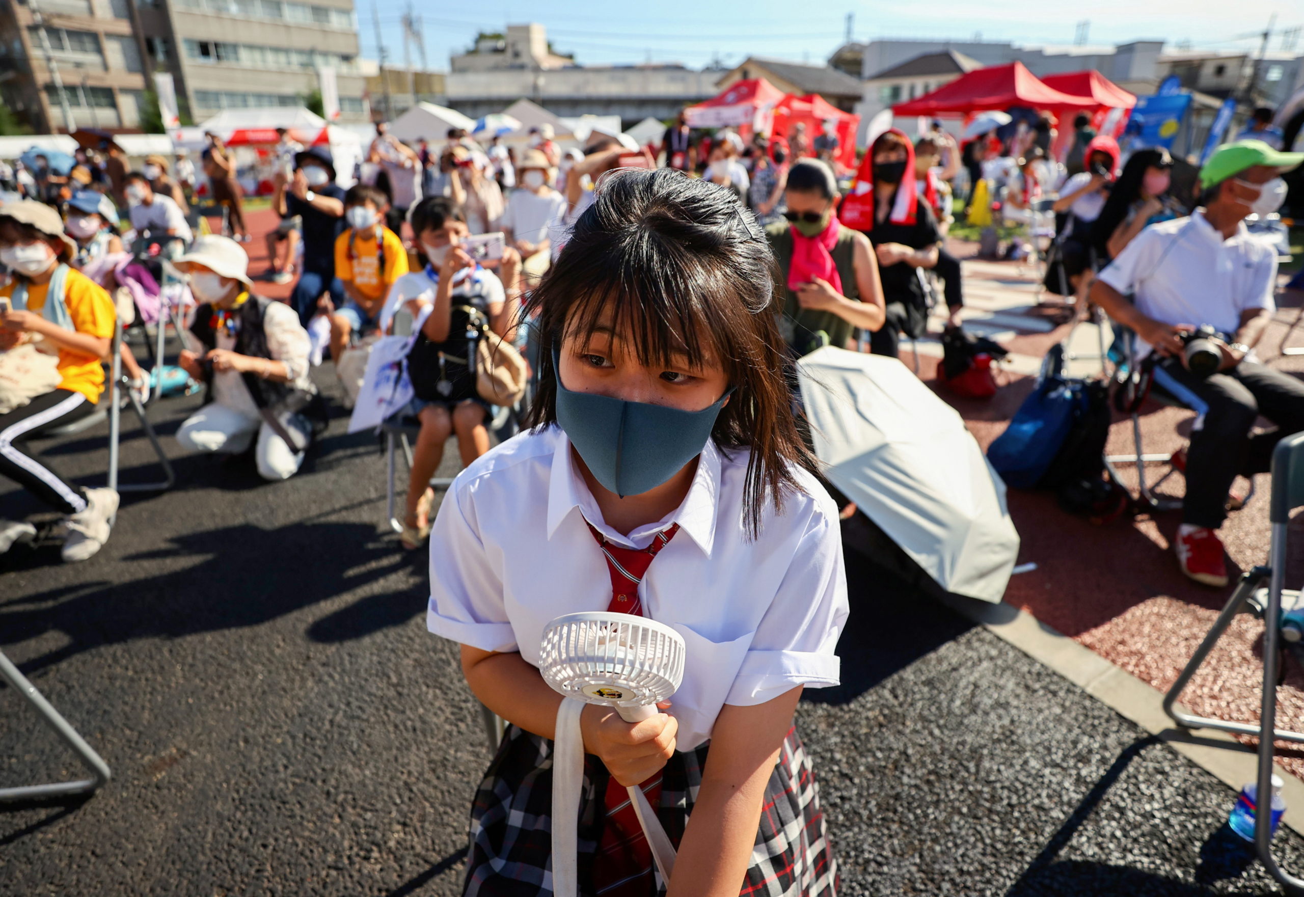 A family member of a torch relay runner wearing a protective mask uses a portable electric fan to cool down as she attends a torch kiss event during Tokyo 2020 Olympic torch relay celebration at Shinagawa Central Park in Tokyo, Japan, 