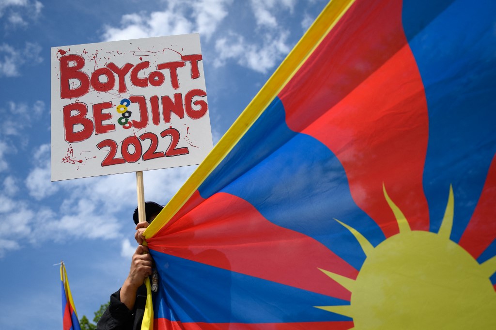 A Tibetan activist holds a placard and a Tibetan flag during a protest against Beijing 2022 Winter Olympics in front of the Olympics Museum in Lausanne on June 23, 2021