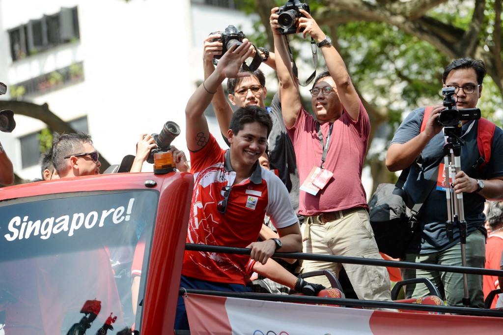 Singapore swimmer Joseph Schooling (on top bus at C) waves to the crowd cheering at his home neighbourhood in Marine Terrace in Singapore on August 18, 2016. - Singapore's Olympic gold medallist Joseph Schooling went on a victory parade through Singapore on August 18, from an open-top bus to meet and greet fans. 