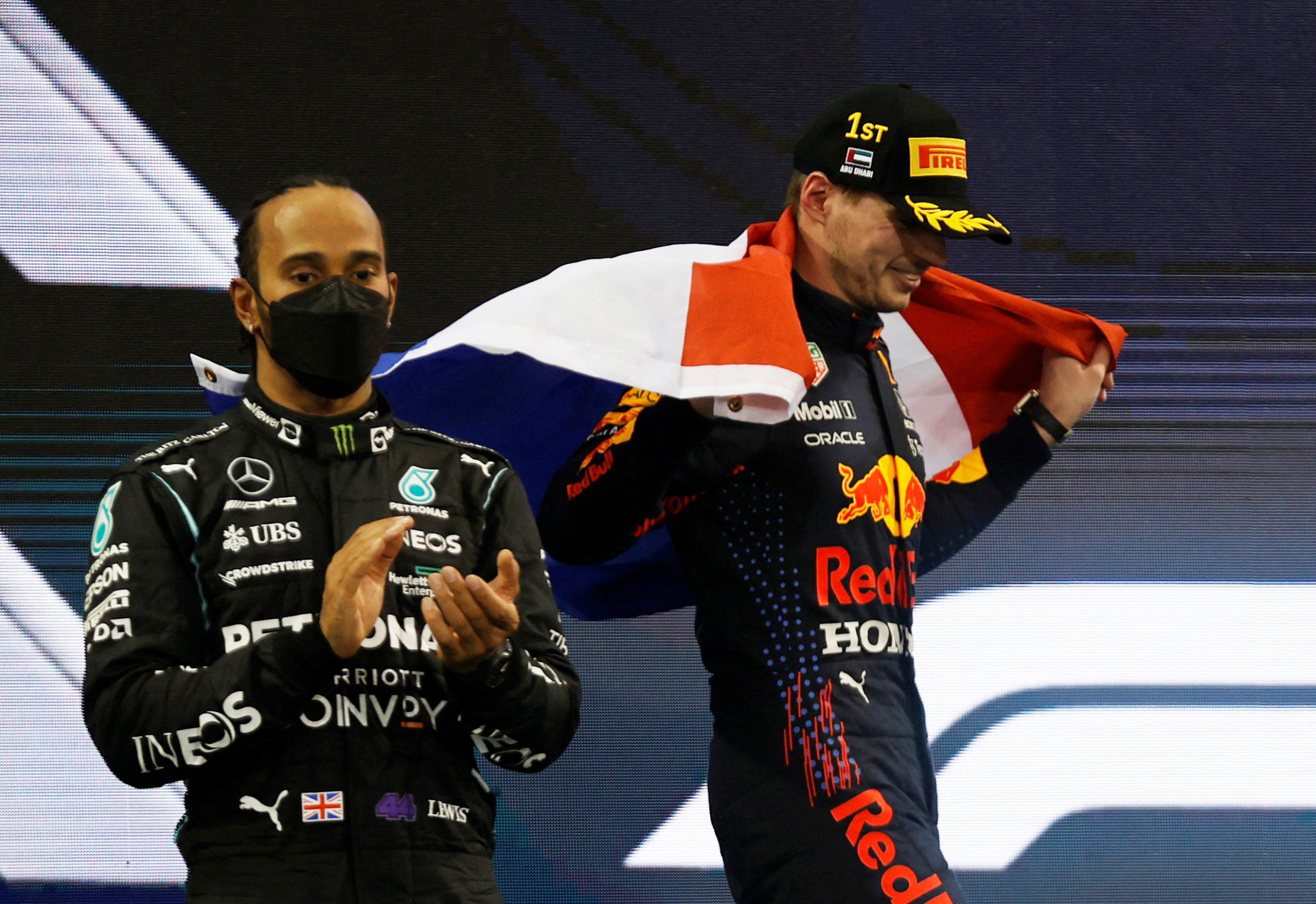 Formula One F1 - Abu Dhabi Grand Prix - Yas Marina Circuit, Abu Dhabi, United Arab Emirates - December 12, 2021 Red Bull's Max Verstappen celebrates winning the race and the world championship with the Netherlands flag on the podium as Mercedes' Lewis Hamilton looks on after finishing second 