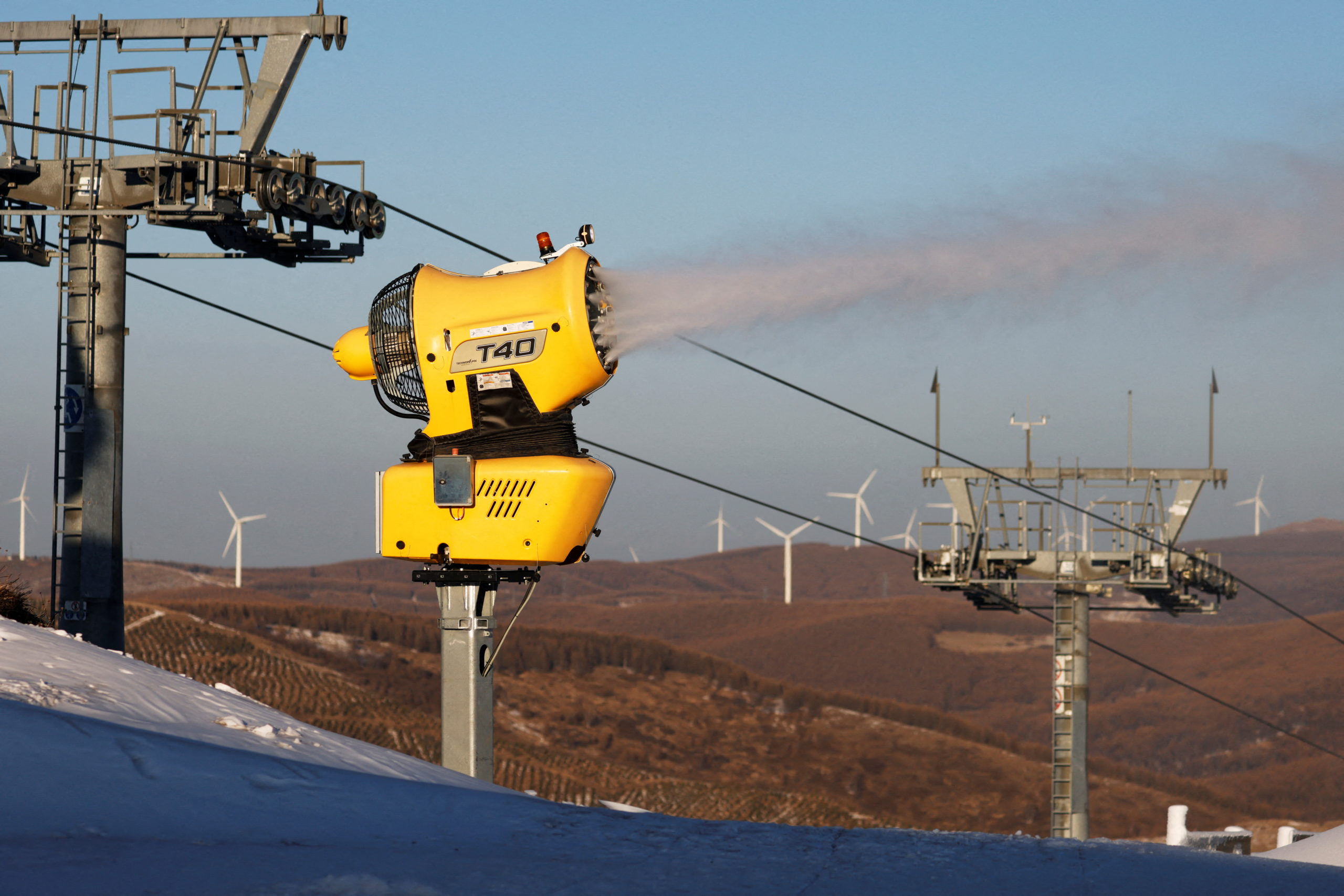 Wind turbines stand behind a snow gun operating at Genting Snow Park during a government-organised media tour to Beijing 2022 Winter Olympics venues in Zhangjiakou, Hebei province, China December 21, 2021. REUTERS/Carlos Ga