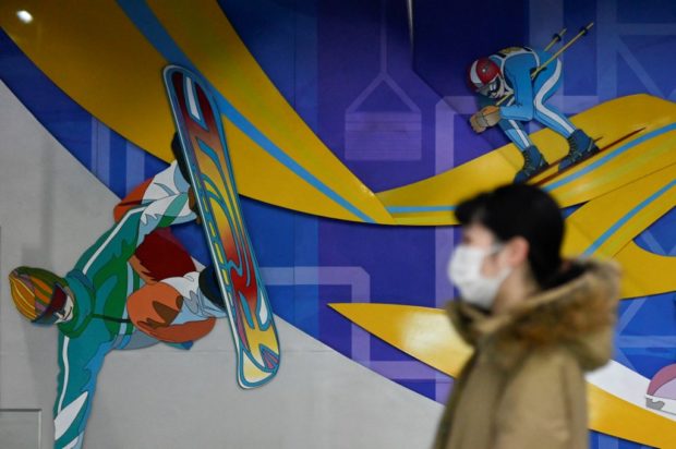 A woman walks past images of snow sports ahead of the Beijing 2022 Winter Olympic Games at a subway station in Beijing on January 6, 2022.