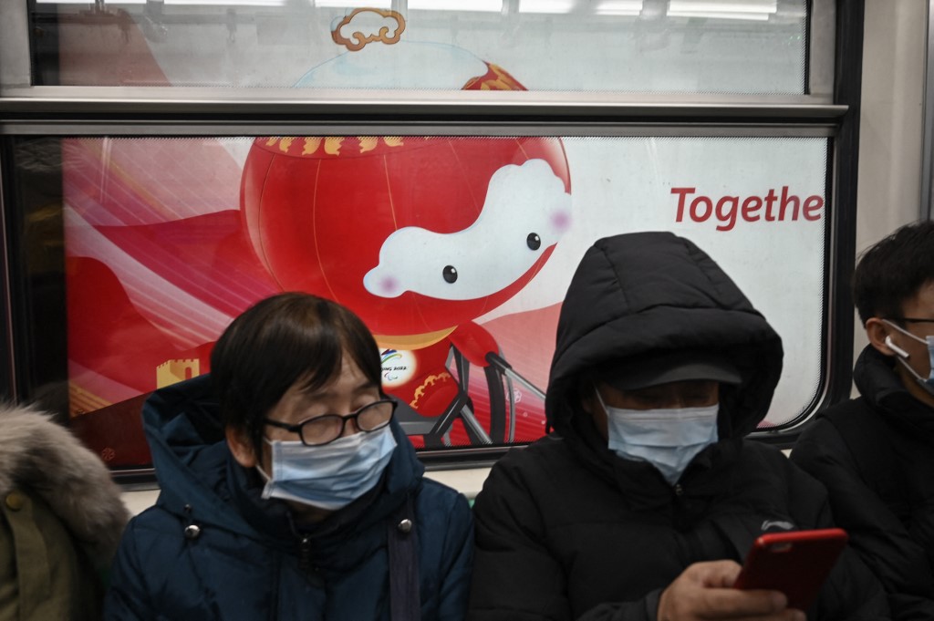 People commute on a train in front of a billboard of Shuey Rhon Rhon, mascot for the Beijing 2022 Paralympic Games, in Beijing on January 26, 2022.