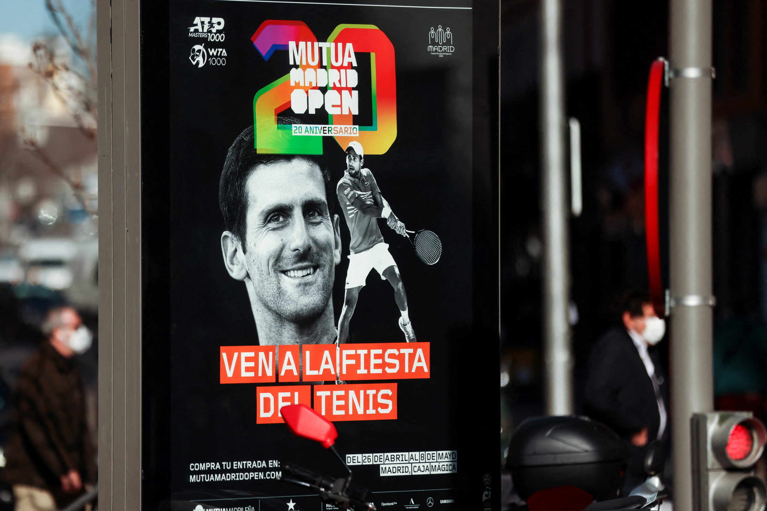 People wearing protective face masks walk past a poster with the image of tennis player Novak Djokovic announcing the Madrid Open, in Madrid, Spain January 18, 2022. REUTERS/Nacho Do