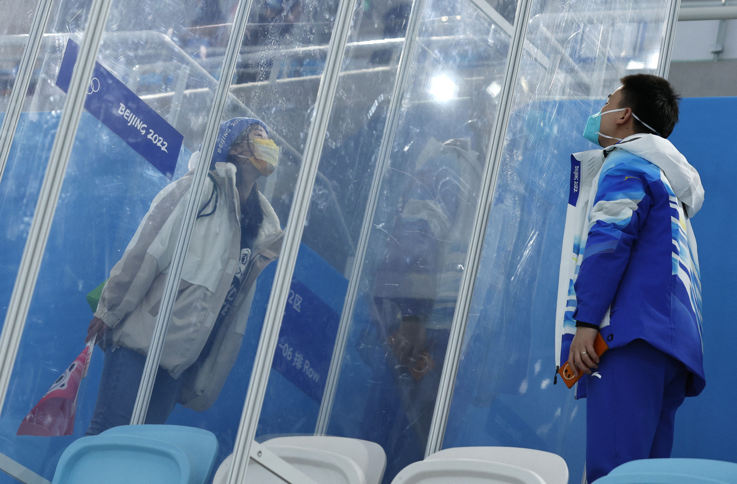 2022 Beijing Olympics - Speed Skating - Men's 5000m - National Speed Skating Oval, Beijing, China - February 6, 2022.  Dr. Ding Hongtao, part of the medical staff, blows a kiss to his girlfriend through screens of glass that separate them because of the "closed loop," a coronavirus disease (COVID-19) prevention measure. She got a ticket for the race and he came to the Speed Skating Oval on his day off so they could be together, even through a screen, for the first time in two weeks.