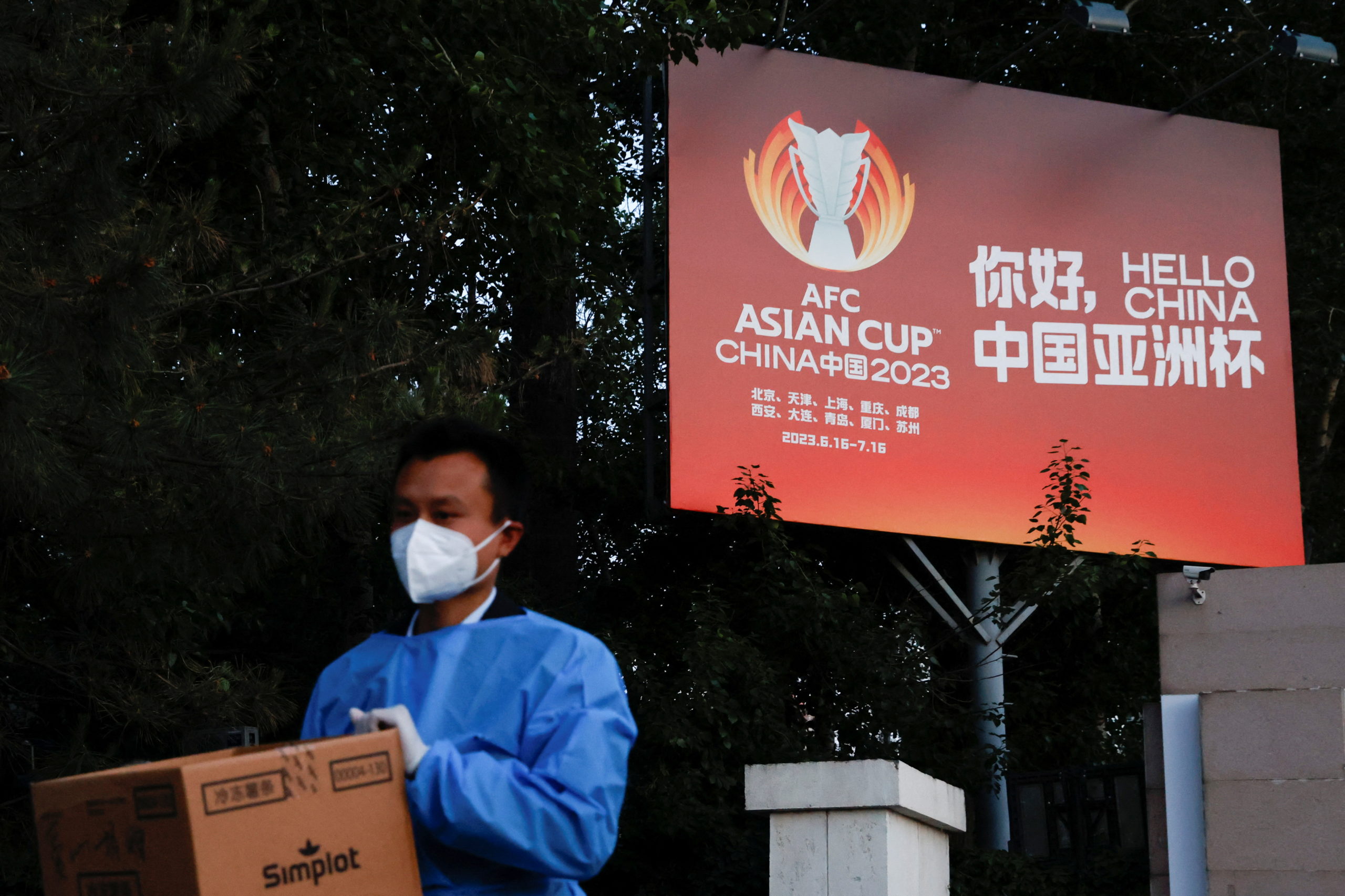 FILE  PHOTO: A man wearing personal protective equipment (PPE) walks past a billboard of the AFC Asian Cup, as he walks out from a makeshift nucleic acid testing site amid the coronavirus disease (COVID-19) outbreak in Beijing, China May 14, 2022. REUTERS/Carlos Garcia Rawlins