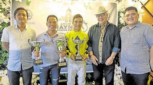 Jockey Jeffril Zarate (center) receives the PSA Cup trophy from PSA representatives Bryan “Slashman” Ulanday of Philippine Star (left) and Randolph Leongson of Spin.ph (right) after steering Time for Glory to victory. With him are trainer Dante Salazar (second from left) and Philracom chair Reli de Leon (second from right). —PHOTO FROM PSA