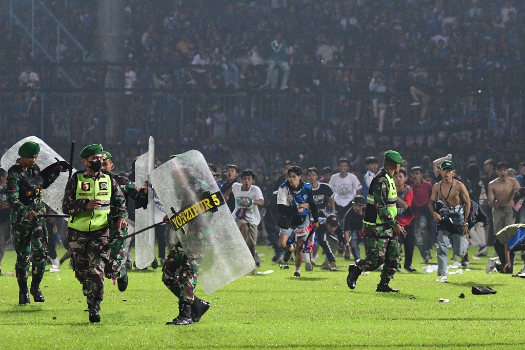 This picture taken on October 1, 2022 shows Arema FC supporters running on the pitch towards members of the Indonesian army after a football match between Arema FC and Persebaya at the Kanjuruhan stadium in Malang, East Java. - Anger against police mounted in Indonesia on October 3 after at least 125 people were killed in one of the deadliest disasters in the history of football, when officers fired tear gas in a packed stadium, triggering a stampede.