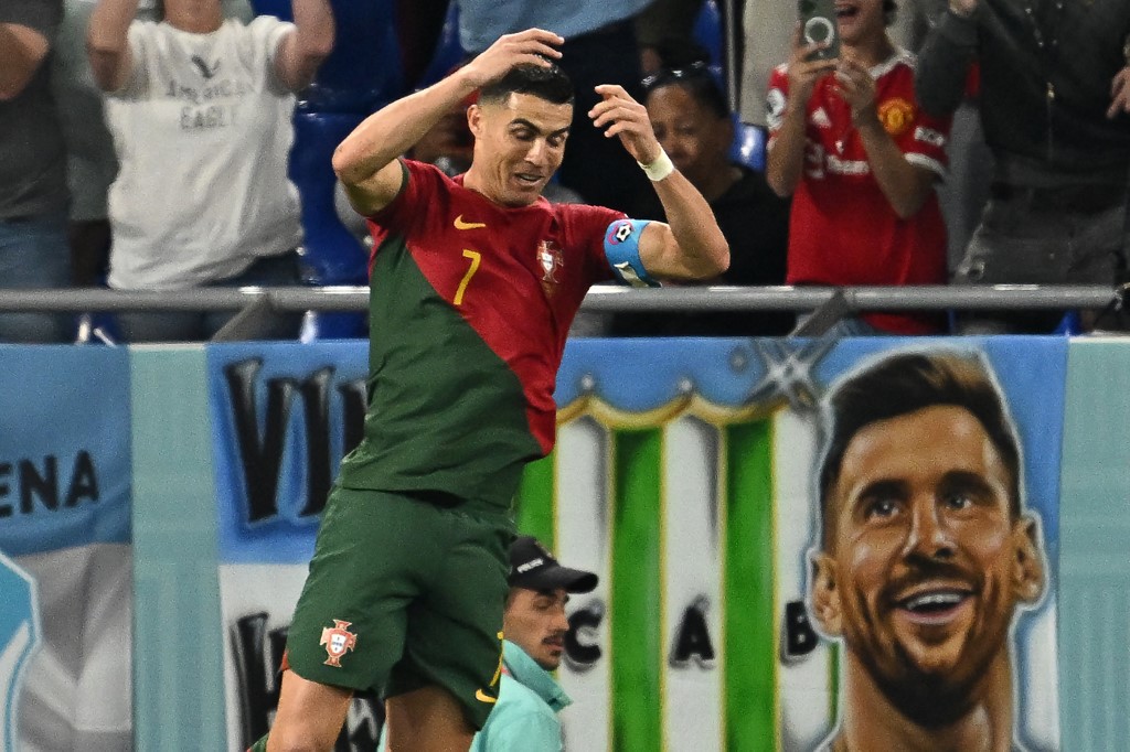 L'attaquant portugais # 07 Cristiano Ronaldo célèbre après avoir marqué le premier but de son équipe depuis le point de penalty alors qu'une bannière représentant l'attaquant argentin Lionel Messi est vue à l'arrière lors du match de football du groupe H de la Coupe du monde Qatar 2022 entre le Portugal et le Ghana au stade 974 à Doha le 24 novembre 2022. 