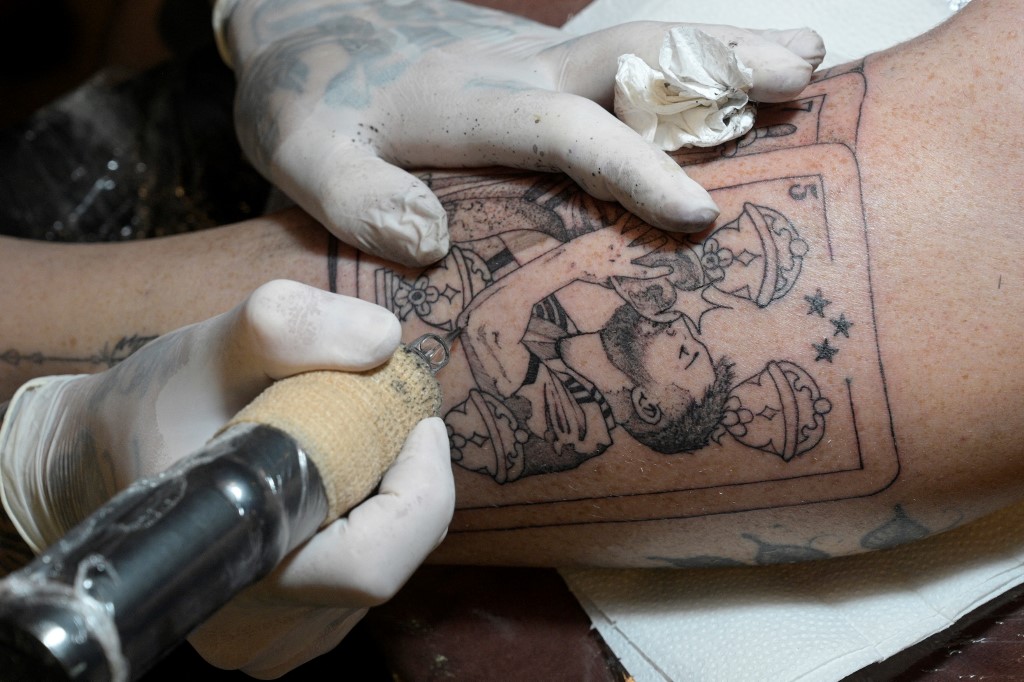 Argentine tattooist Tebi Cobra Vucinovich gets a tattoo of Argentina's forward Lionel Messi kissing the FIFA World Cup trophy on Ariel Sacchi's leg at Ds Tattoo Shop in Buenos Aires on December 23, 2022.