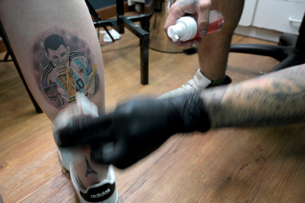Tattooist Dario Vivas protects the tattoo of Argentina's Lionel Messi kissing the FIFA World Cup trophy on the leg of Nicolas Rechanik at Face Tattoo shop in Buenos Aires on December 23, 2022. 