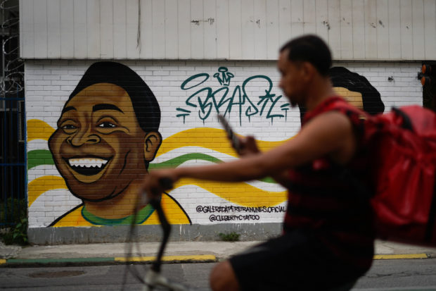 A man rides on a bike past a mural depicting Brazil's late football player Pele at Tijuca neighbourhood in Rio de Janeiro, Brazil, on December 29, 2022, just hours after his passing at a Sao Paulo hospital. - Brazilian football icon Pele, widely regarded as the greatest player of all time and a three-time World Cup winner who masterminded the "beautiful game," died on Thursday at the age of 82. The Albert Einstein hospital treating Pele said in a statement his death after a long battle with cancer was caused by "multiple organ failure." (Photo by Mauro PIMENTEL / AFP)