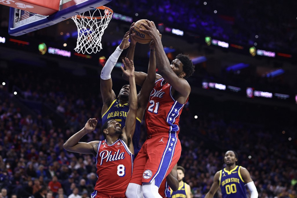 Kevon Looney #5 of the Golden State Warriors, and Joel Embiid #21 and De'Anthony Melton #8 of the Philadelphia 76ers reach for a rebound during the second quarter at Wells Fargo Center on December 16, 2022 in Philadelphia, Pennsylvania. 