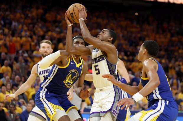  De'Aaron Fox #5 of the Sacramento Kings drives on Kevon Looney #5 and Stephen Curry #30 of the Golden State Warriors in the second half of Game Six of the Western Conference First Round Playoffs at Chase Center on April 28, 2023 in San Francisco, California. 