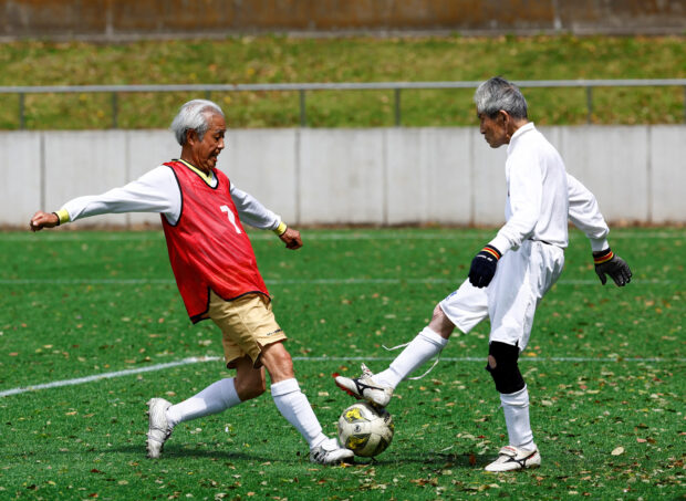 FILE PHOTO: Red Star’s midfielder Mutsuhiko Nomura (left), 83, shoots to score a goal against Blue Hawai’s goalkeeper Hiroshi Nishino, 87, at the SFL (Soccer For Life) 80 League opening match in Tokyo, Japan, April 12, 2023. 