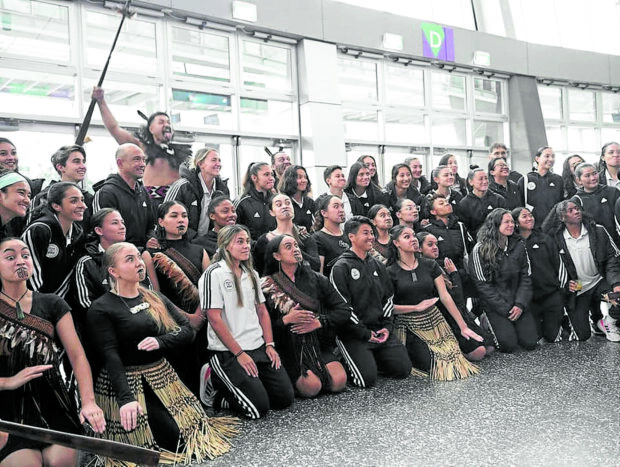 Miembros del equipo de fútbol femenino de Filipinas, incluidas Sofia Harrison (primera fila con camiseta blanca) y Olivia McDaniel (tercera fila, cuarta desde la izquierda) posan con miembros de la comunidad maorí para la tradicional ceremonia de bienvenida de Nueva Zelanda conocida como 