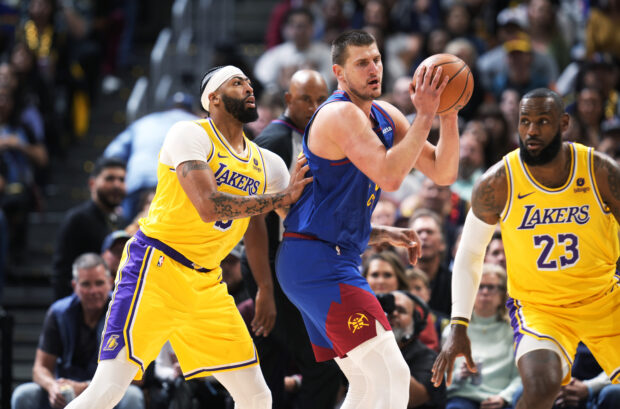 Denver Nuggets center Nikola Jokic, center, looks to pass the ball as Los Angeles Lakers forward Anthony Davis, left, and forward LeBron James defend during the first half of an NBA basketball game Tuesday, Oct. 24, 2023, in Denver.