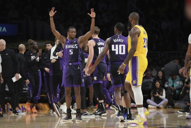 Sacramento Kings guard De'Aaron Fox, left, celebrates with forward Harrison Barnes, center, as Los Angeles Lakers forward LeBron James looks on after a timeout was called during the first half of an NBA basketball game Wednesday, Nov. 15, 2023, in Los Angeles. 