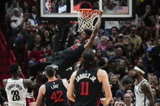 Miami Heat forward Jimmy Butler (22) swings from the rim after dunking during the second half of an NBA basketball game against the Brooklyn Nets, Thursday, Nov. 16, 2023, in Miami.
