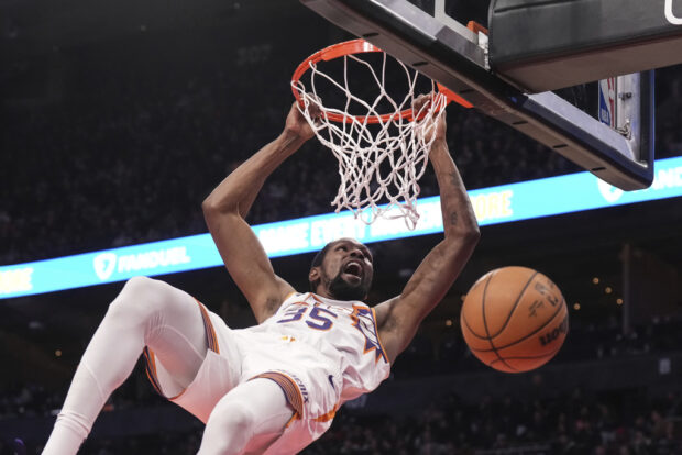 Phoenix Suns' Kevin Durant hangs from the hoop after scoring against the Toronto Raptors during the second half of an NBA basketball game in Toronto on Wednesday, Nov. 29, 2023. 