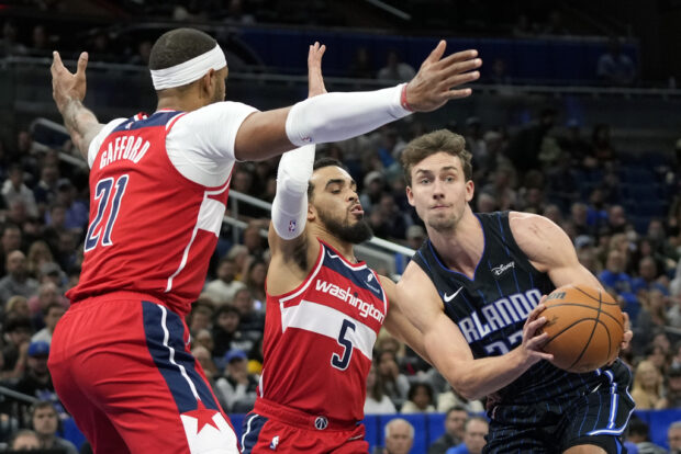 Orlando Magic forward Franz Wagner, right, looks to pass the ball as his path to the basket is blocked by Washington Wizards guard Tyus Jones (5) and center Daniel Gafford (21) during the first half of an NBA basketball game Friday, Dec. 1, 2023, in Orlando, Florida.