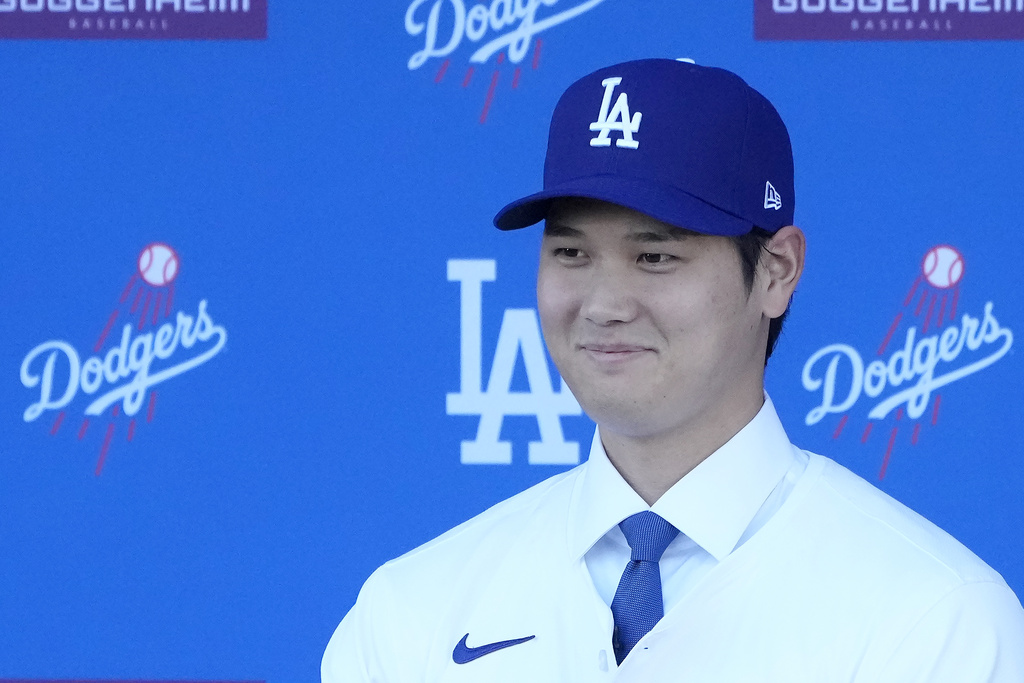 Los Angeles Dodgers' Shohei Ohtani smiles while wearing a jersey and baseball cap during a news conference at Dodger Stadium Thursday, Dec. 14, 2023, in Los Angeles.
