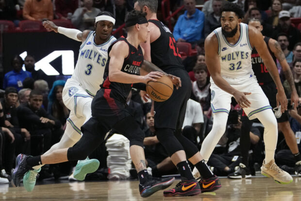 Miami Heat guard Tyler Herro, center, drives to the basket as Minnesota Timberwolves forward Jaden McDaniels (3) and center Karl-Anthony Towns (32) defend during the first half of an NBA basketball game, Monday, Dec. 18, 2023, in Miami. 