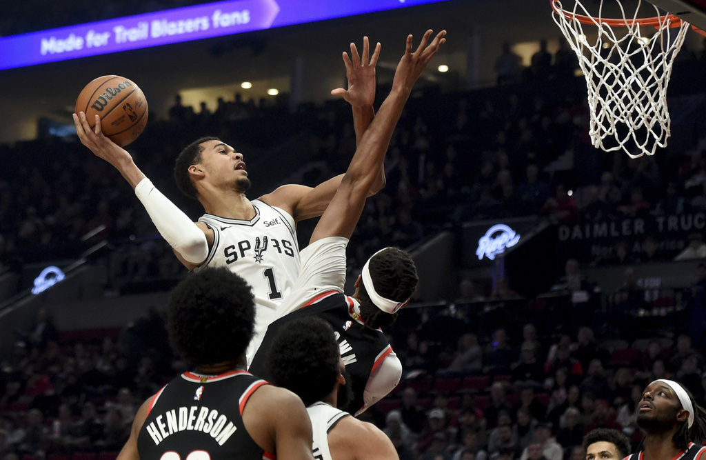 San Antonio Spurs center Victor Wembanyama, left, drives to the basket against Portland Trail Blazers center Moses Brown, center, as forward Jerami Grant, right, watches during the first half of an NBA basketball game in Portland, Ore., Thursday, Dec. 28, 2023