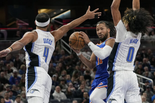 New York Knicks guard Jalen Brunson, center, passes the ball between Orlando Magic guards Jalen Suggs (4) and Anthony Black (0) during the first half of an NBA basketball game, Friday, Dec. 29, 2023, in Orlando, Florida.