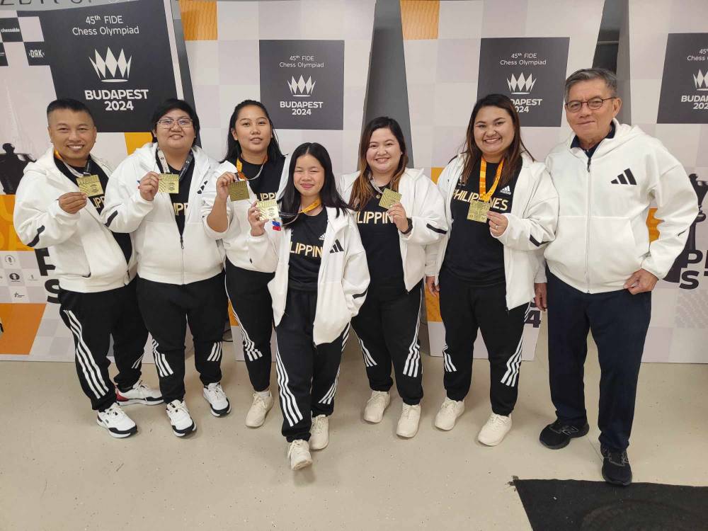 Grandmasters Jayson Gonzales (left) and Eugene Torre, the country’s chess icon, bookend the women’s team as its members—( from 2nd left) Shania Mae Mendoza, Janelle Mae Frayna, Ruelle Canino, Bernadette Galas and Jan Jodilyn Fronda— flaunt their gold medals. —CONTRIBUTED PHOTO