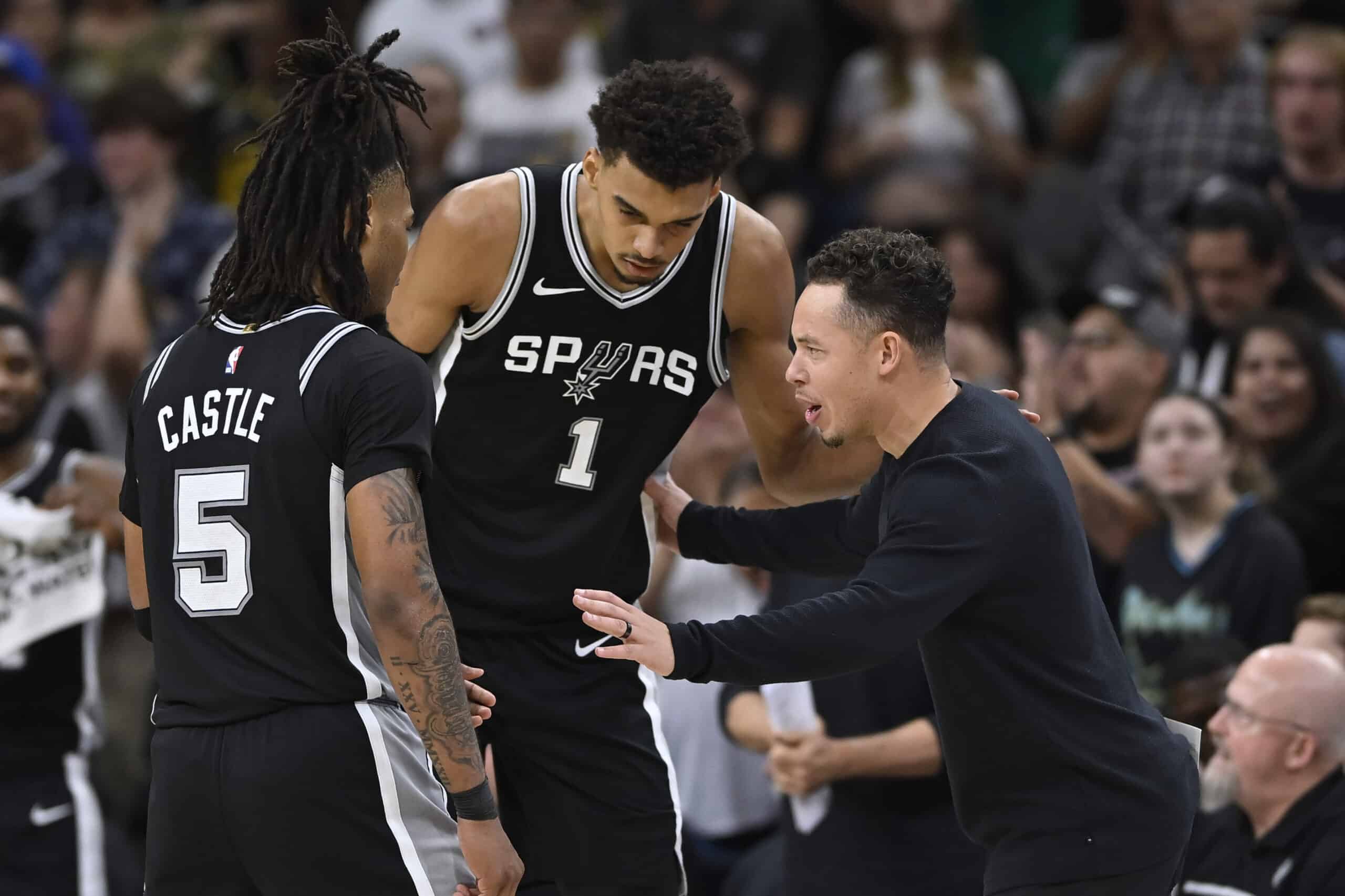 San Antonio Spurs acting head coach Mitch Johnson, right, speaks with Spurs players Victor Wembanyama (1) and Stephon Castle  NBA Warriors