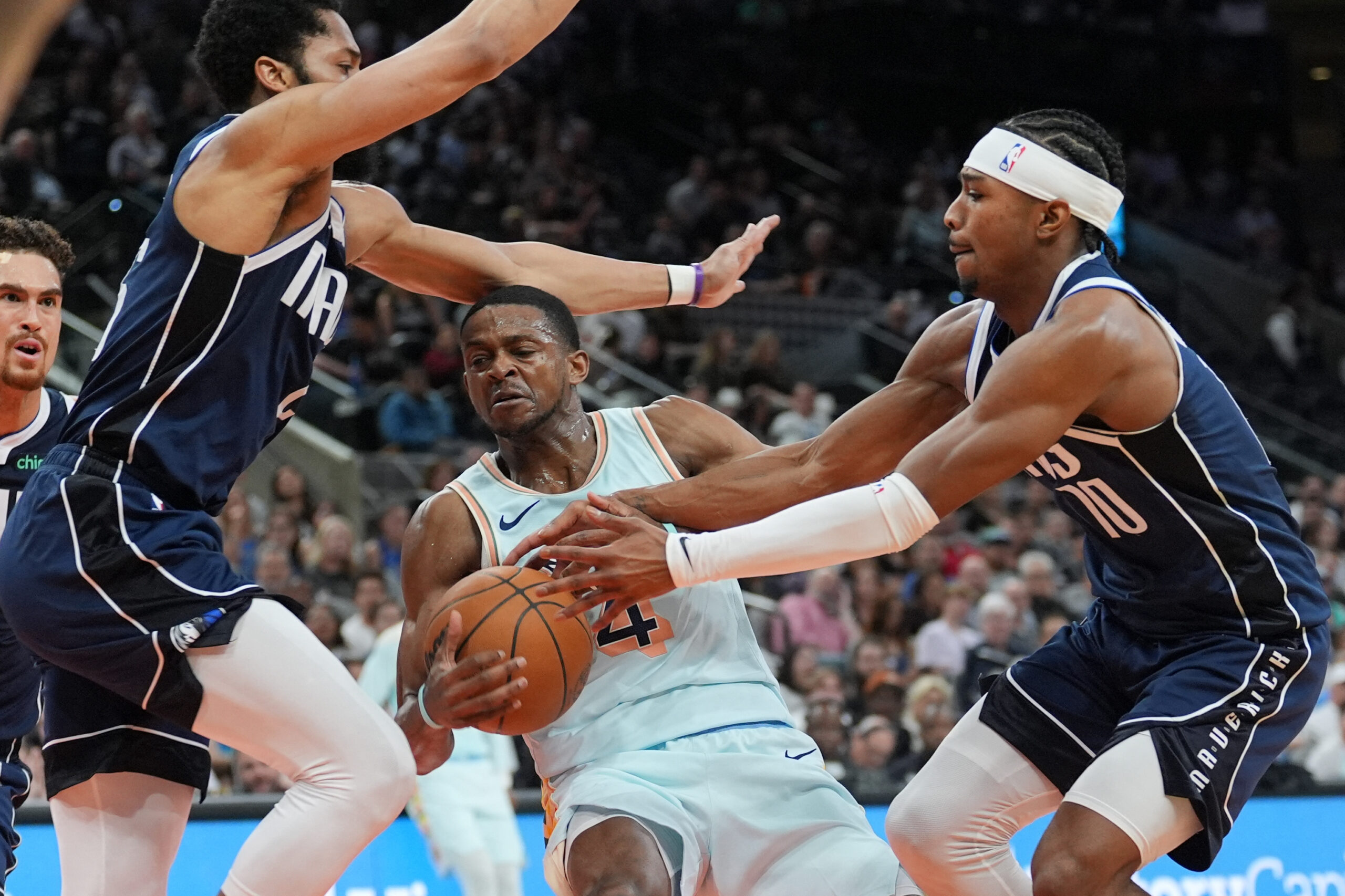 NBA 12 de marzo de 2025; San Antonio, Texas, EE. UU.; El guardia de San Antonio Spurs De'aaron Fox (4) tiene el balón contra los Guardias de Dallas Mavericks Spencer Dinwiddie (26) y Brandon Williams (10) en la primera mitad en Frost Bank Center. 